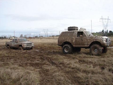 1996 Ford Bronco - A heavily mud-covered 1996 Ford Bronco tows a stuck pickup truck out of a muddy field.