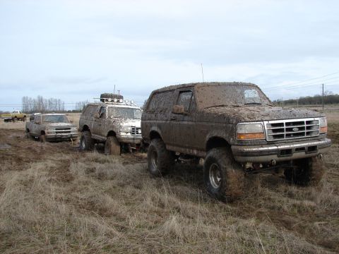 1996 Ford Bronco - Several off-road vehicles are covered in mud after driving through a wet field.
