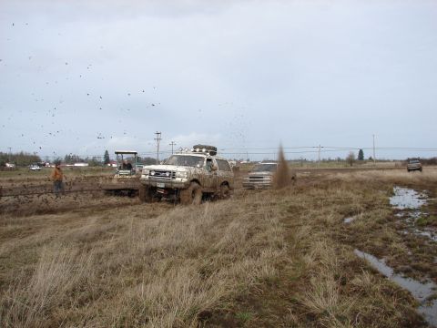1996 Ford Bronco - A white Ford Bronco navigates a muddy terrain, kicking up dirt as it goes.