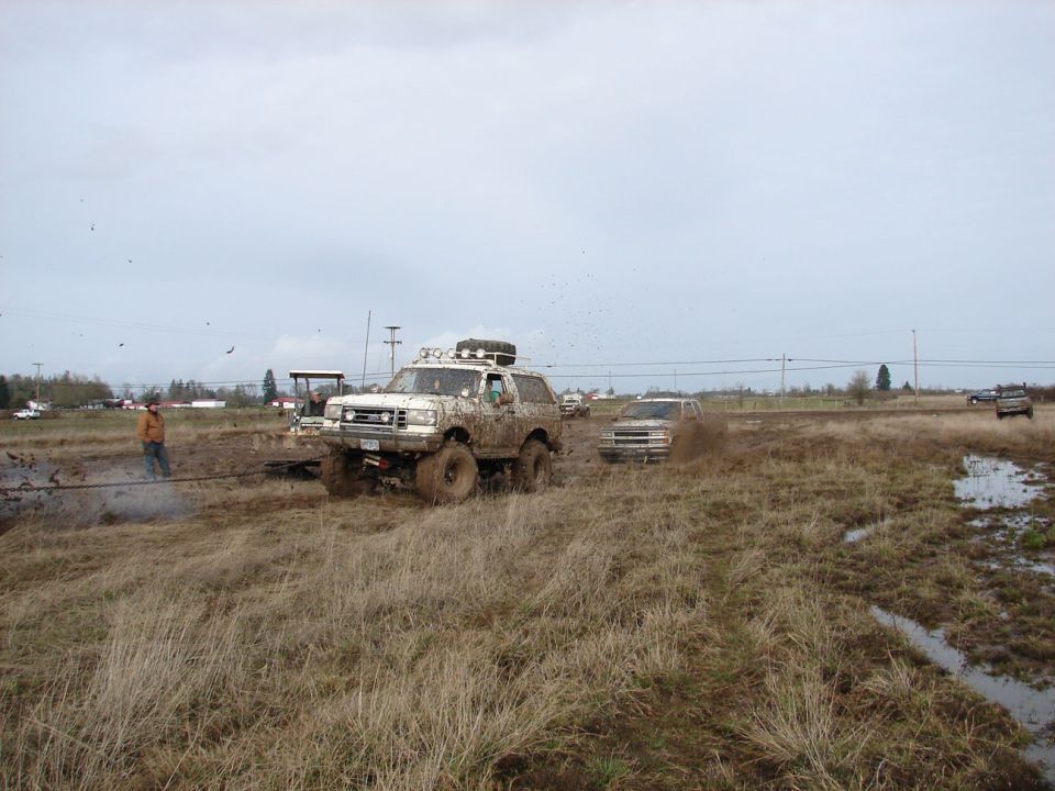 White 1996 Ford Bronco navigating a muddy off-road course with other vehicles visible