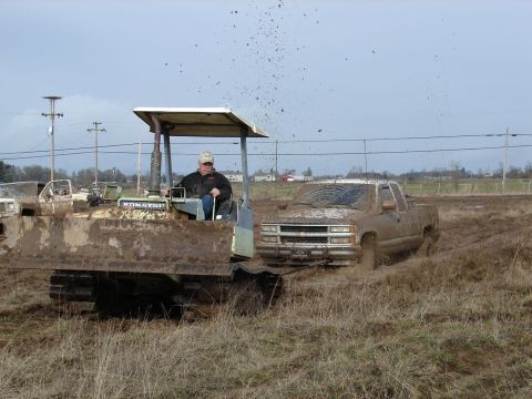 1996 Ford Bronco - A muddy pickup truck is stuck in the mud next to a bulldozer, with mud flying through the air.