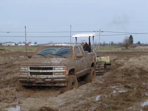 1996 Ford Bronco - A muddy pickup truck navigates through a very muddy field, with a tracked attachment behind it.