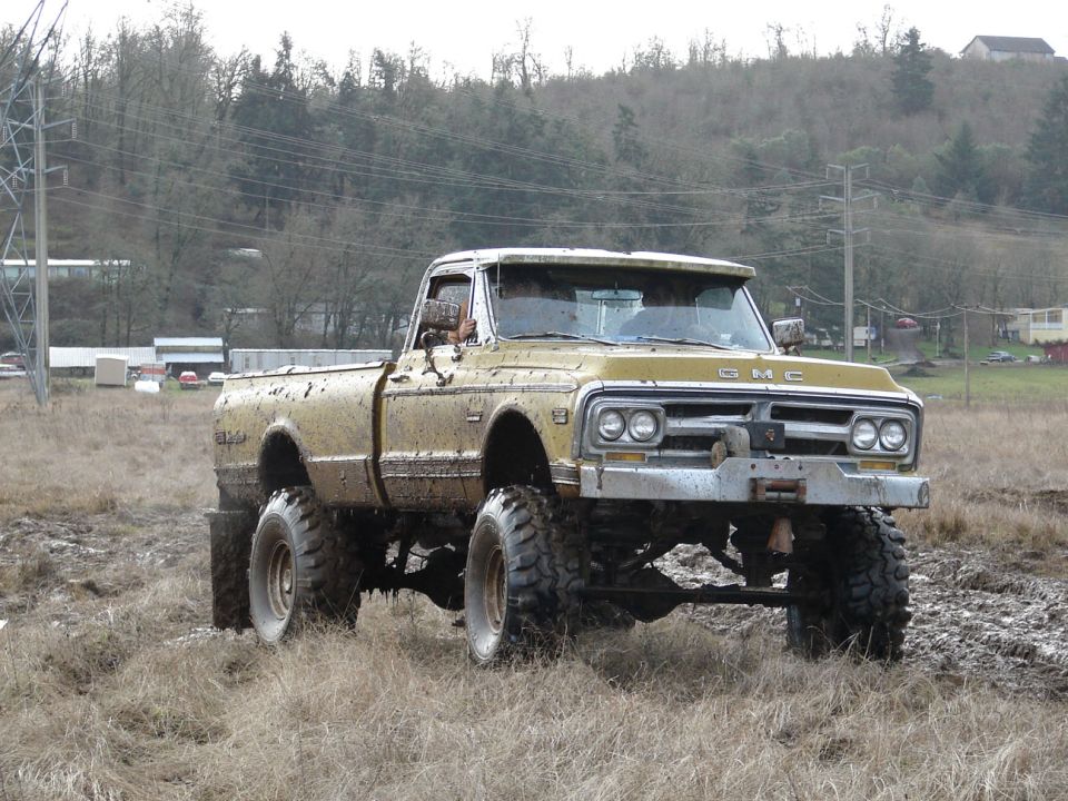 Muddy gold lifted GMC pickup on large off-road tires in a muddy field