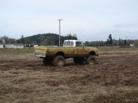 1996 Ford Bronco - A lifted yellow pickup truck navigates a muddy field under an overcast sky.
