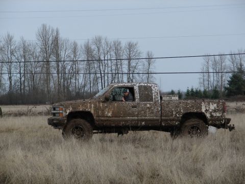 1996 Ford Bronco - Muddy pickup truck navigates a grassy field under an overcast sky.