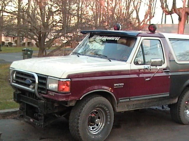 Ford Bronco with a two-tone paint job and a brush guard. A sticker on the windshield reads 'Muddy Adventures'