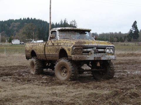 1996 Ford Bronco - This heavily mud-caked pickup truck, likely from the 1970s, is stuck in a muddy field.