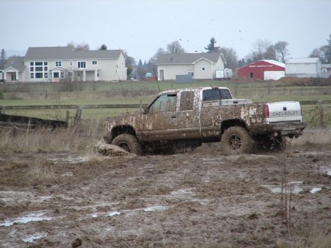 1996 Ford Bronco - A white Chevrolet pickup truck is stuck in thick mud, with mud splattering around it. The rear Chevrolet badging is visible.