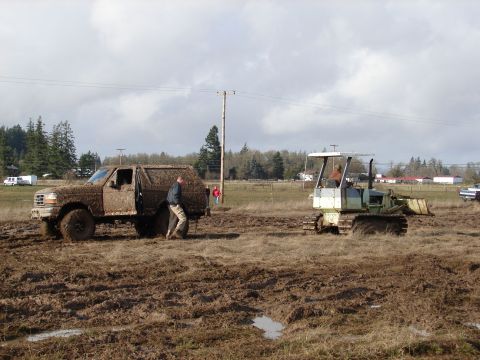 1996 Ford Bronco - A muddy pickup truck is stuck in a field while a bulldozer operates nearby.