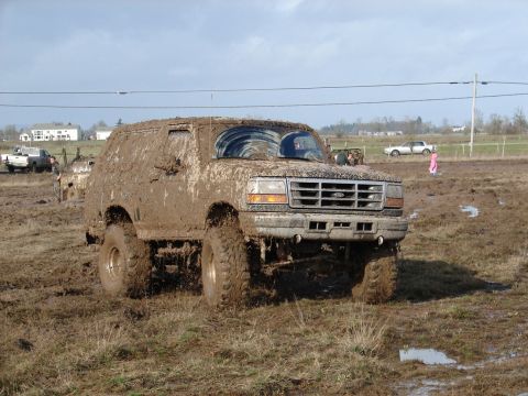 1996 Ford Bronco - This heavily muddied SUV, likely a 1992 model, navigates a challenging off-road terrain.