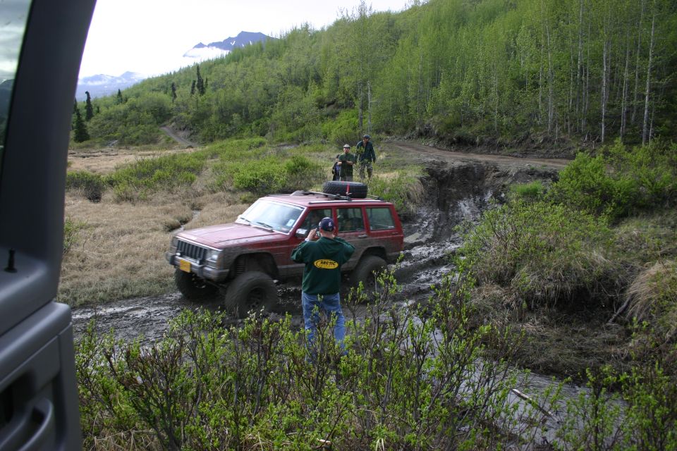 Red Jeep Cherokee XJ navigating a muddy trail with two people watching