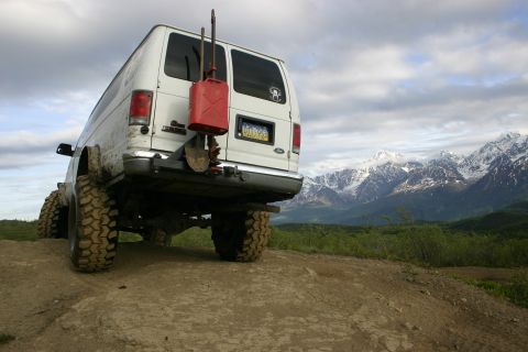 2003 Jeep TJ - Modified van with off-road tires parked on a dirt track with snowy mountains in the distance.