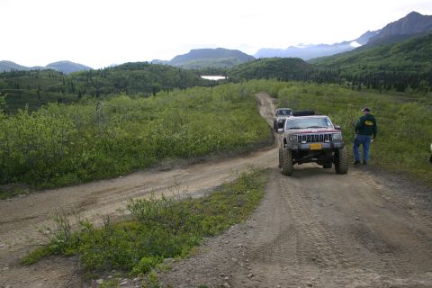 2003 Jeep TJ - A group of Jeeps, including a red Cherokee, navigate a winding dirt road through a lush, green landscape.