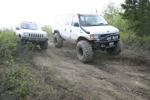 2003 Jeep TJ - Two modified off-road vehicles navigate a dirt path through brush and trees.