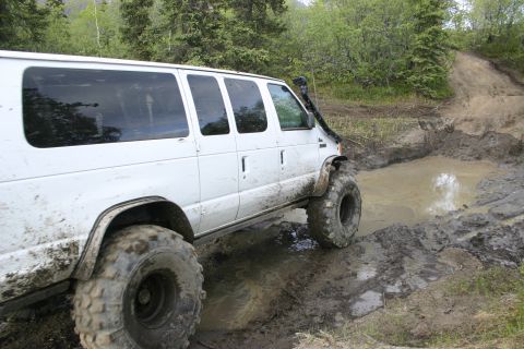2003 Jeep TJ - A white van with oversized tires and a snorkel attachment attempts to traverse a challenging muddy terrain.