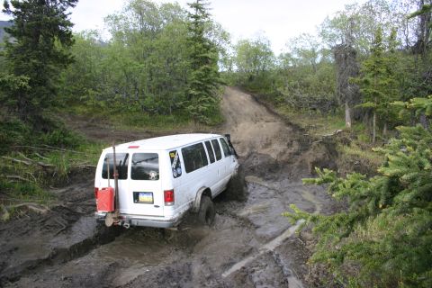 2003 Jeep TJ - A white van navigates a difficult muddy path, with a gas can and shovel attached to its rear.