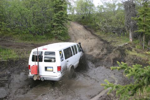 2003 Jeep TJ - A white van navigates a muddy off-road trail, kicking up spray as it goes.