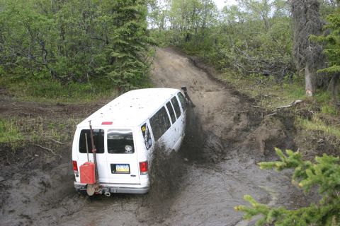 2003 Jeep TJ - A white van navigates a challenging muddy trail, kicking up dirt and water.