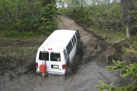 2003 Jeep TJ - Van struggling through thick mud on an off-road trail with trees on either side.
