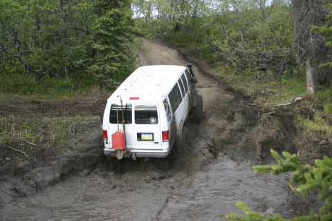2003 Jeep TJ - A white van navigates a challenging muddy off-road path, kicking up water and mud.