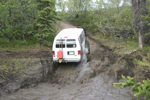 2003 Jeep TJ - A white van navigates a muddy off-road trail, kicking up dirt and water.