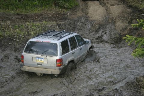 2003 Jeep TJ - A silver Jeep Grand Cherokee tackles a challenging muddy off-road course, demonstrating its 4x4 capabilities.