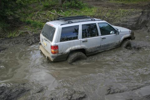 2003 Jeep TJ - This Jeep Grand Cherokee appears to be from the late 1990s, not a 2003 model, as it navigates a muddy off-road obstacle.