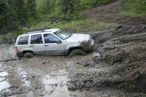 2003 Jeep TJ - A silver 1999 Jeep Grand Cherokee is deeply stuck in a muddy off-road trail.