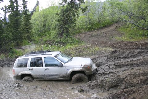 2003 Jeep TJ - A Jeep Grand Cherokee navigates a difficult muddy trail, getting stuck in the mire.