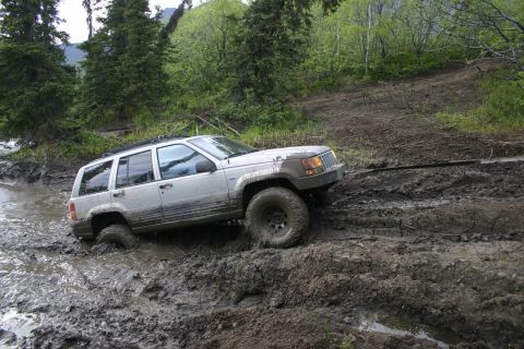 2003 Jeep TJ - A silver Jeep Grand Cherokee navigates a muddy trail, with its front wheel submerged in water.