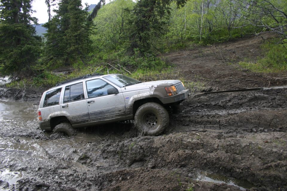 Silver Jeep Grand Cherokee stuck in mud, front wheel deep in water