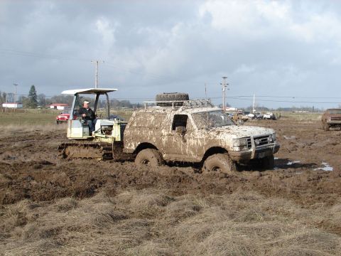 1996 Ford Bronco - Muddy 1996 Ford Bronco and a tracked vehicle are stuck in a muddy field under a cloudy sky.