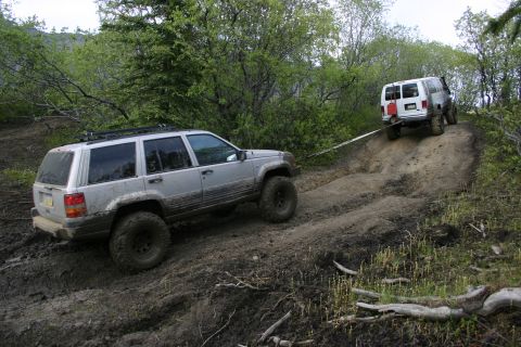 2003 Jeep TJ - Two off-road vehicles navigate a challenging muddy incline, with one vehicle assisting the other.
