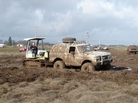 1996 Ford Bronco - A muddy 1996 Ford Bronco is stuck in a field, with a tractor assisting it.