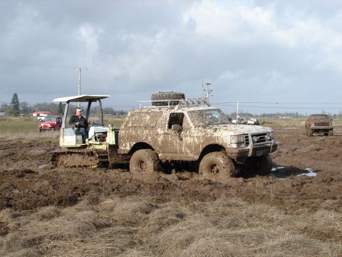 1996 Ford Bronco - A white SUV is stuck in the mud, with a bulldozer nearby and other vehicles in the background.