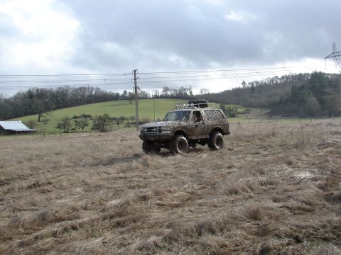 1996 Ford Bronco - Muddy 1996 Ford Bronco navigating a rough, grassy field under an overcast sky.