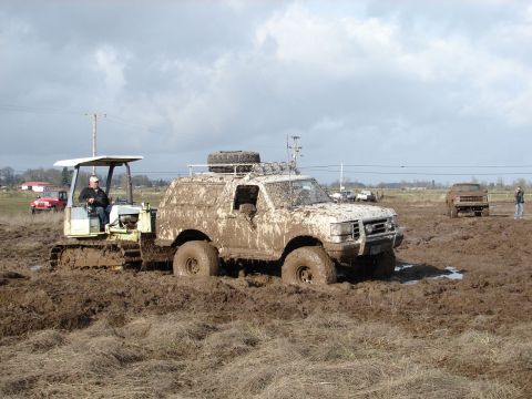 1996 Ford Bronco - Off-road vehicles are stuck in the mud, with a tractor assisting.