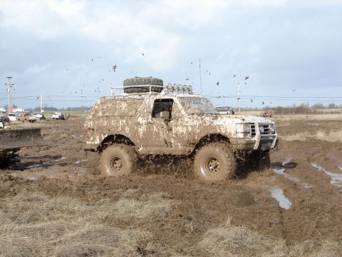 1996 Ford Bronco - This 1996 Ford Bronco is shown navigating a challenging muddy terrain, kicking up dirt as it goes.
