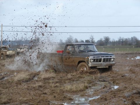 1996 Ford Bronco - Several trucks are seen playing in the mud, with one in the foreground creating a large splash.