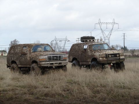 1996 Ford Bronco - Two 1996 Ford Broncos are seen covered in mud after an off-roading excursion, with power lines visible in the background.
