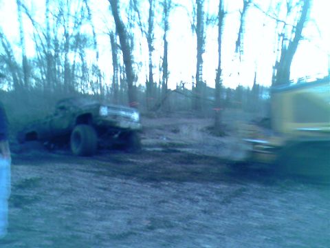 1976 GMC C/K Pickup - A muddy pickup truck is stuck in the dirt, with another vehicle blurred in the background.