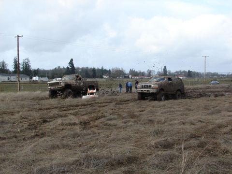 1996 Ford Bronco - Two muddy trucks navigate a field, with a pickup truck visible in the distance under an overcast sky.