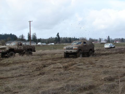 1996 Ford Bronco - Several off-road vehicles are navigating a muddy field under an overcast sky.