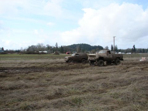 1996 Ford Bronco - Two off-road vehicles, a 1996 Ford Bronco and a pickup truck, navigate a muddy field under a cloudy sky.
