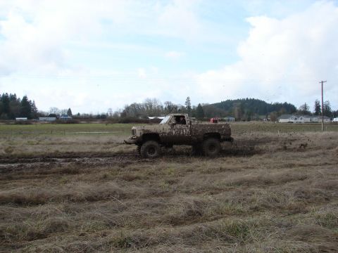 1996 Ford Bronco - This heavily mud-splattered pickup truck navigates a wet, grassy field under a cloudy sky.