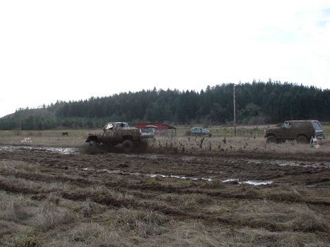 1996 Ford Bronco - Multiple vehicles are seen driving through a muddy field with a barn and trees in the background.