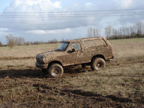 1996 Ford Bronco - This 1996 Ford Bronco is heavily covered in mud while navigating a rough, grassy terrain.