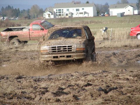 1996 Ford Bronco - A 1996 Ford Bronco navigates a muddy terrain, kicking up spray as it goes.