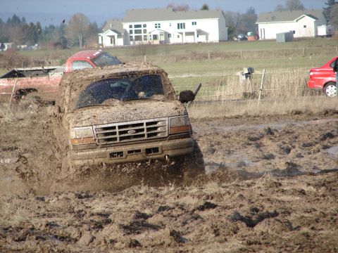 1996 Ford Bronco - This 1996 Ford Bronco is navigating a challenging muddy terrain, with other vehicles visible in the background.
