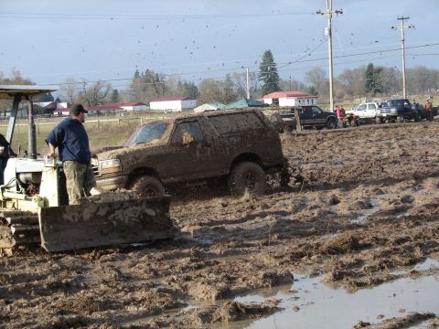1996 Ford Bronco - A muddy SUV is stuck in a mud pit, with a bulldozer assisting and other trucks waiting in the background.